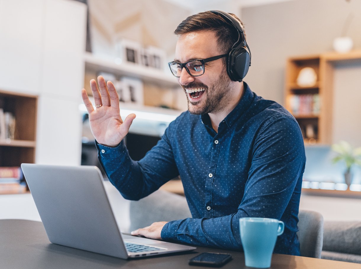 Man sitting in front of his laptop greeting a person
