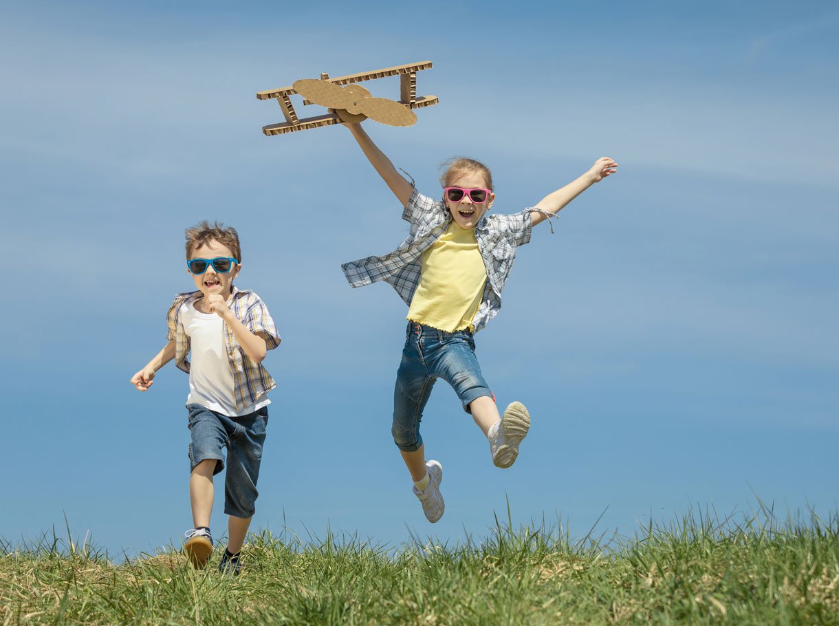 A boy and a girl play with a cardboard propeller plane
